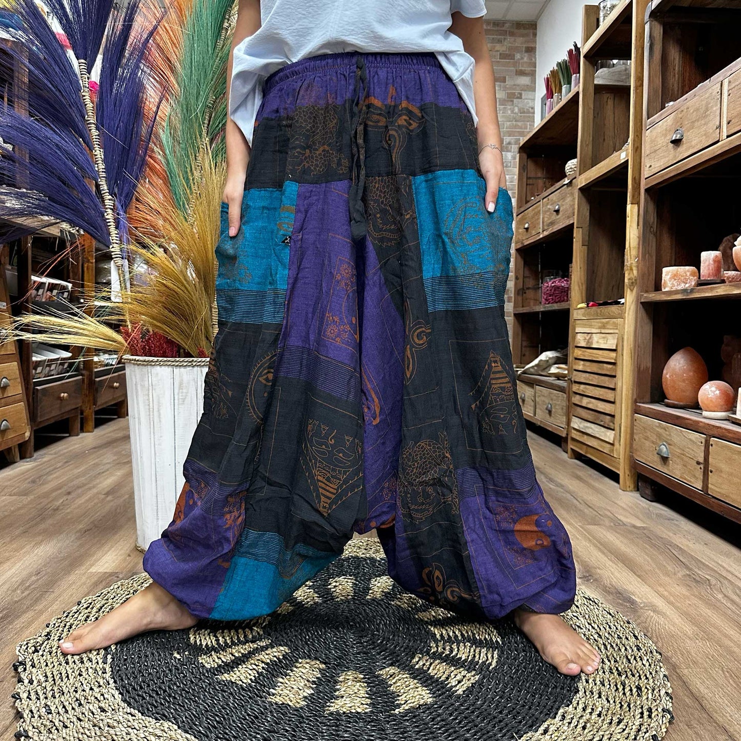 Samsara Wellbeing Aladdin style yoga pants in black, purple and blue patchwork worn by a barefoot person indoors
