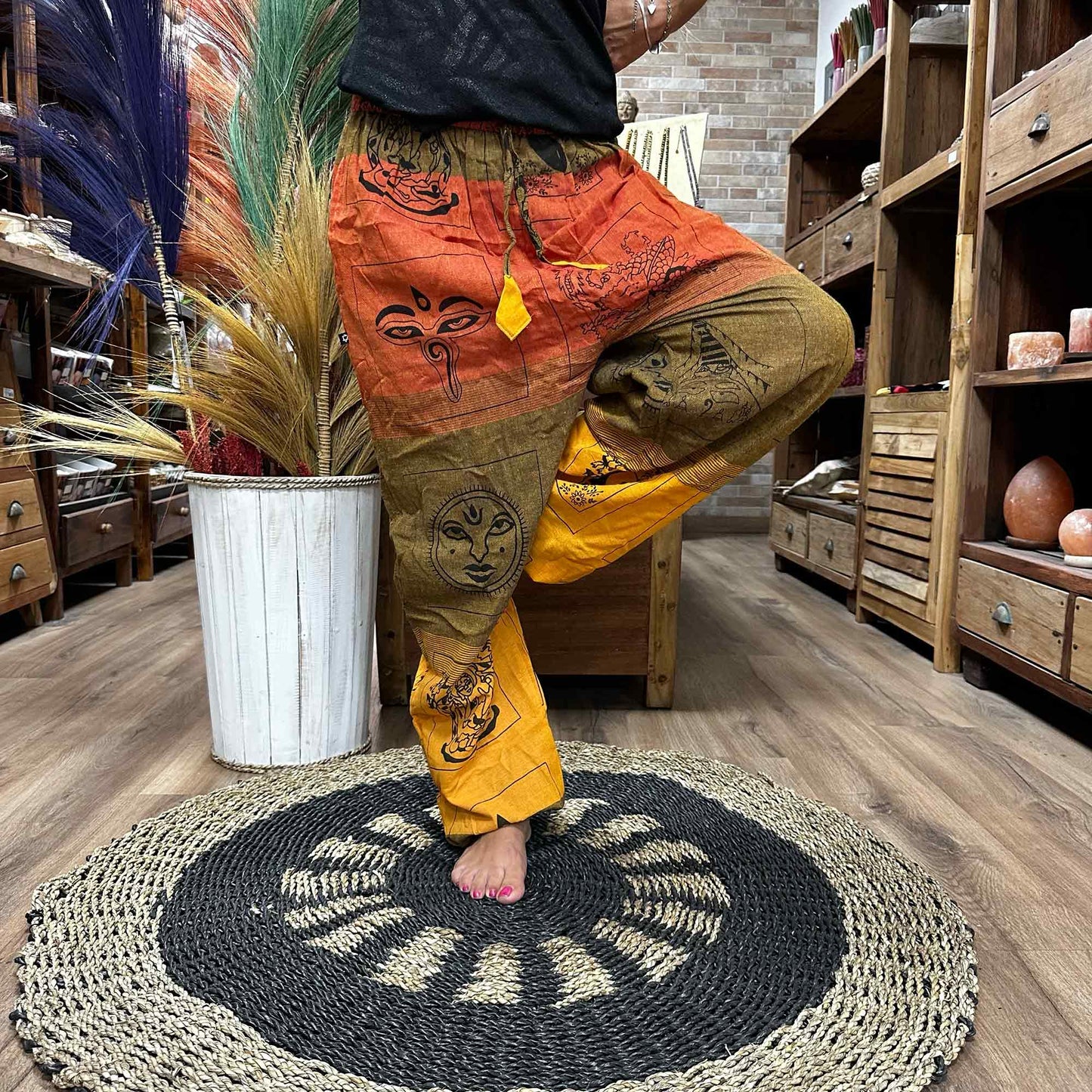 Samsara Wellbeing Himalayan print yoga pants with vibrant orange, brown, and yellow shades worn during a yoga pose in a cozy room