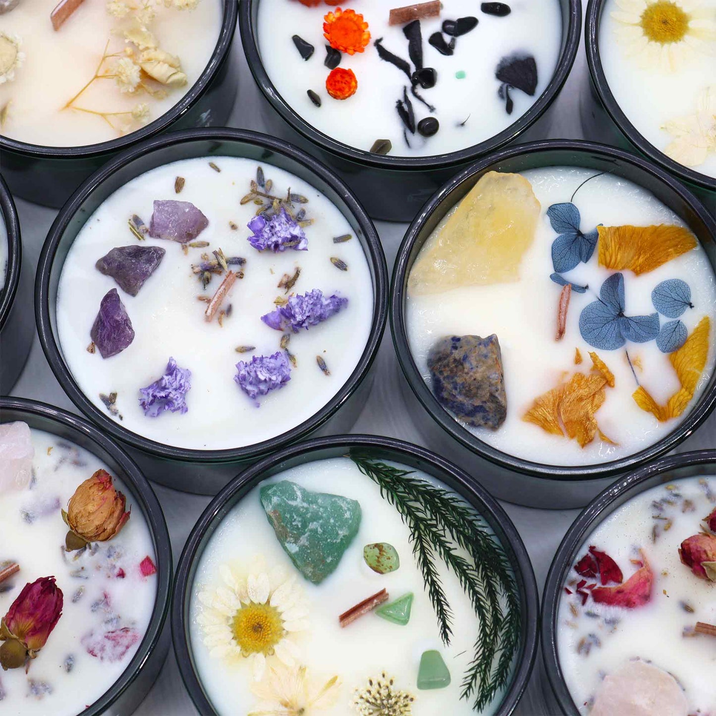 Collection of aromatherapy candle with crystals featuring various dried flowers and colourful stones in black containers