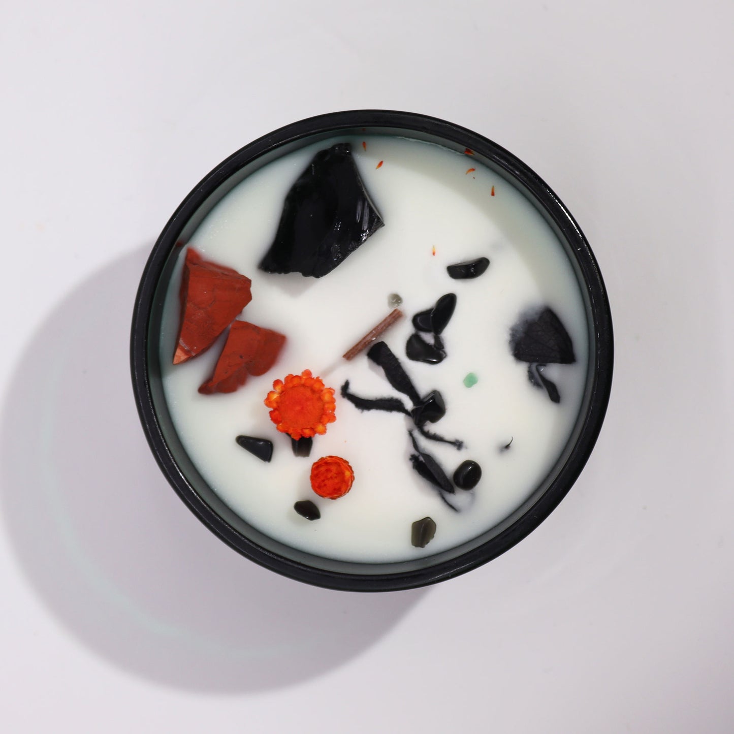 Top view of a crystal infused candle with white wax and embedded black and orange crystals in a black container