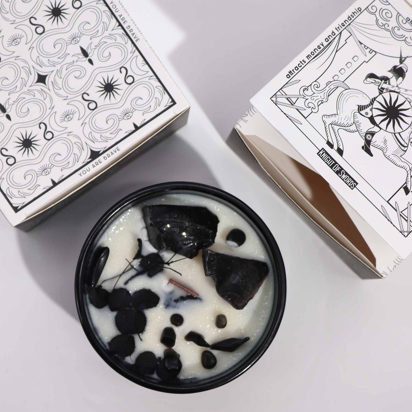 Crystal infused flower candle in black container with large dark crystals and decorative white packaging