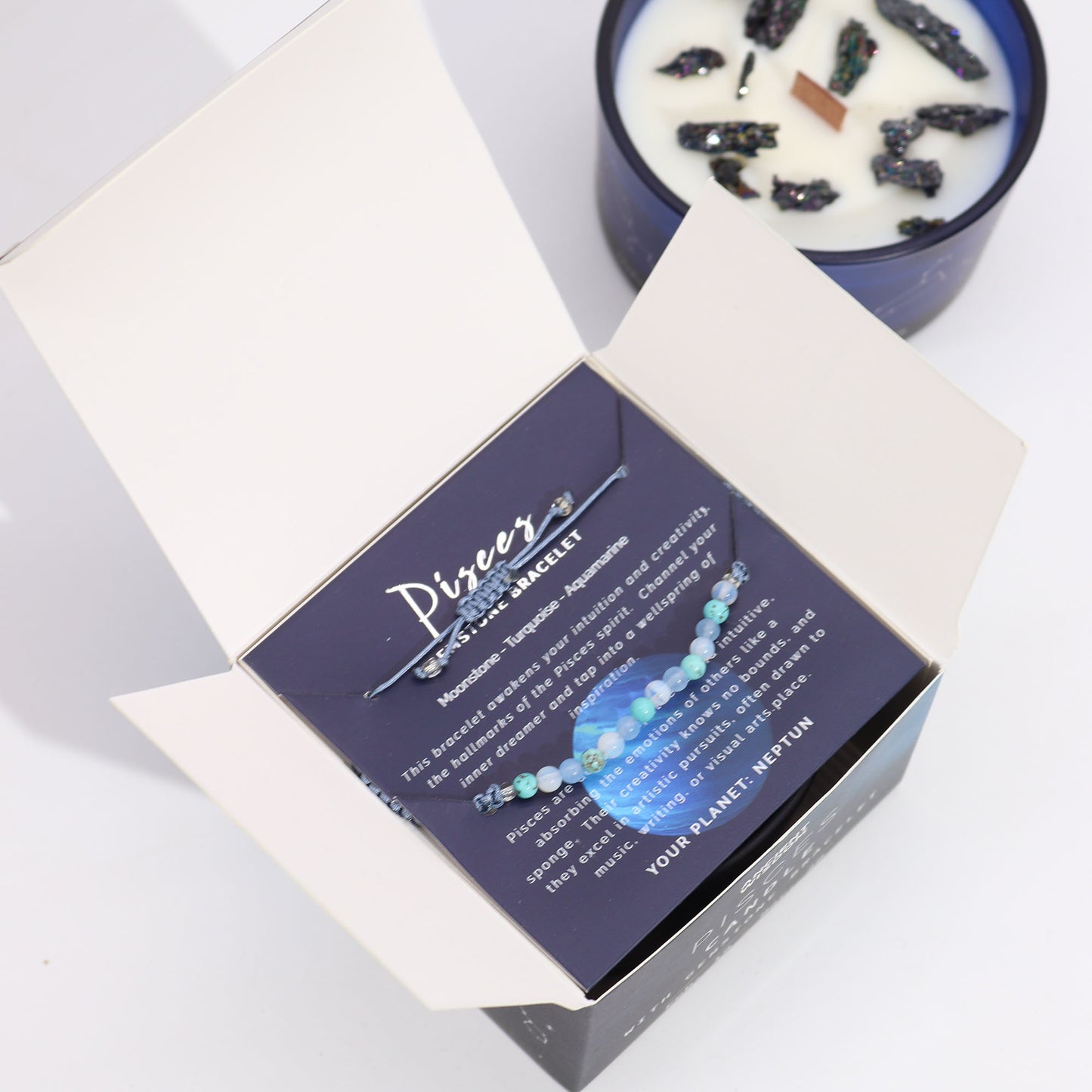 Samsara Wellbeing Pisces crystal candle in blue holder with crystals on white wax next to an open box