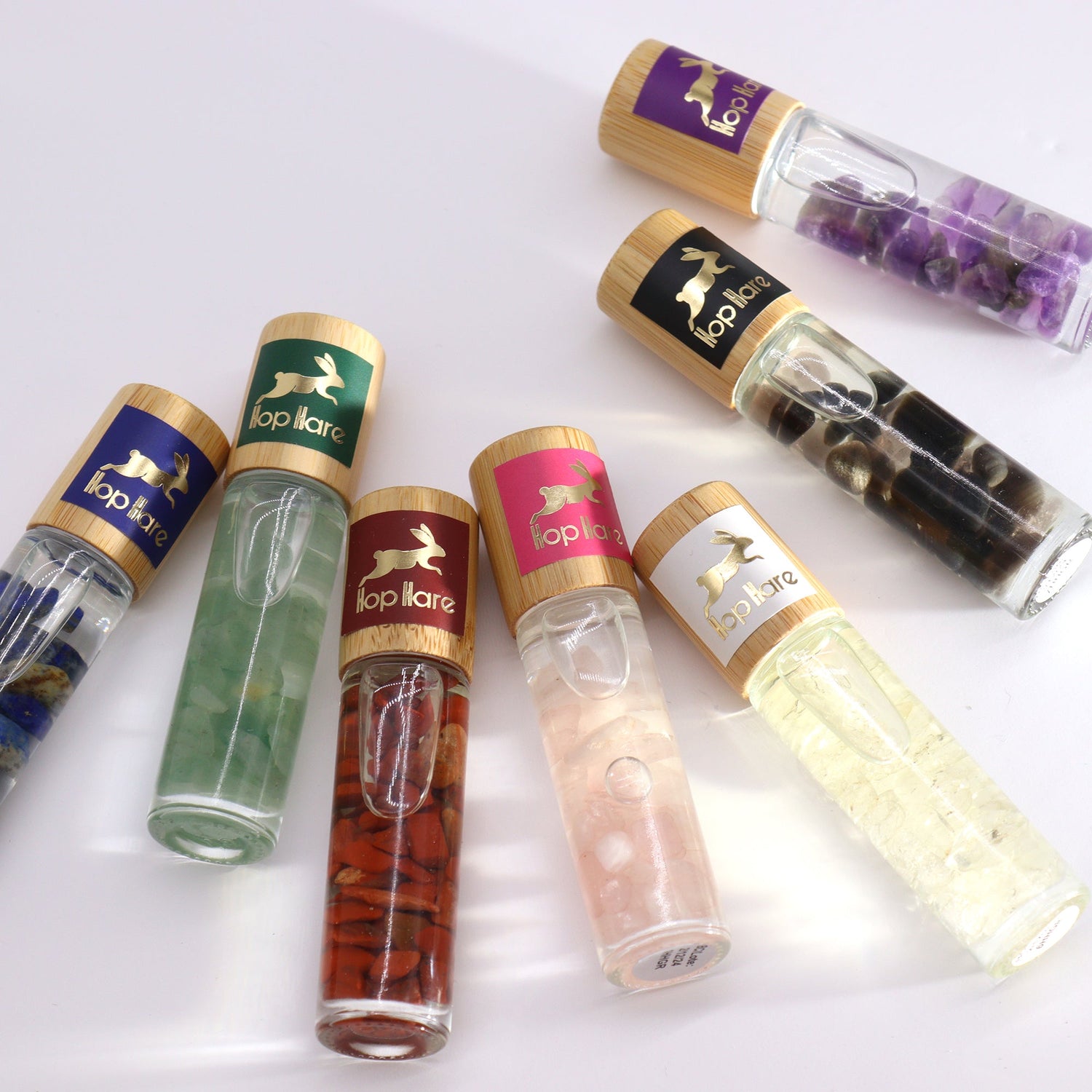 Hop Hare essential oil roll on collection with gemstone-infused bottles and wooden caps arranged on white background