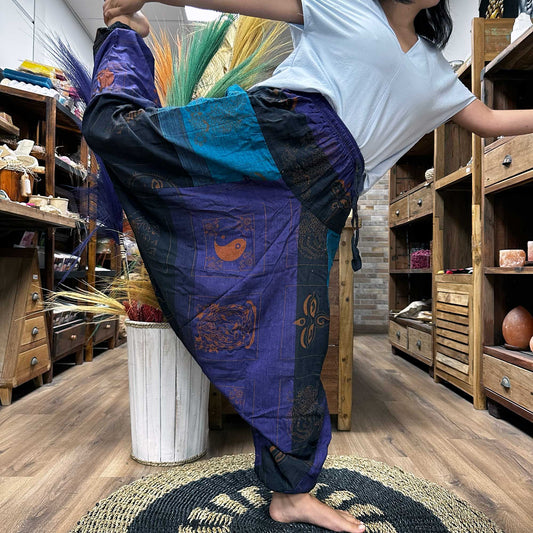 Person wearing colourful Aladdin style yoga pants by Samsara Wellbeing stretching indoors on wooden floor