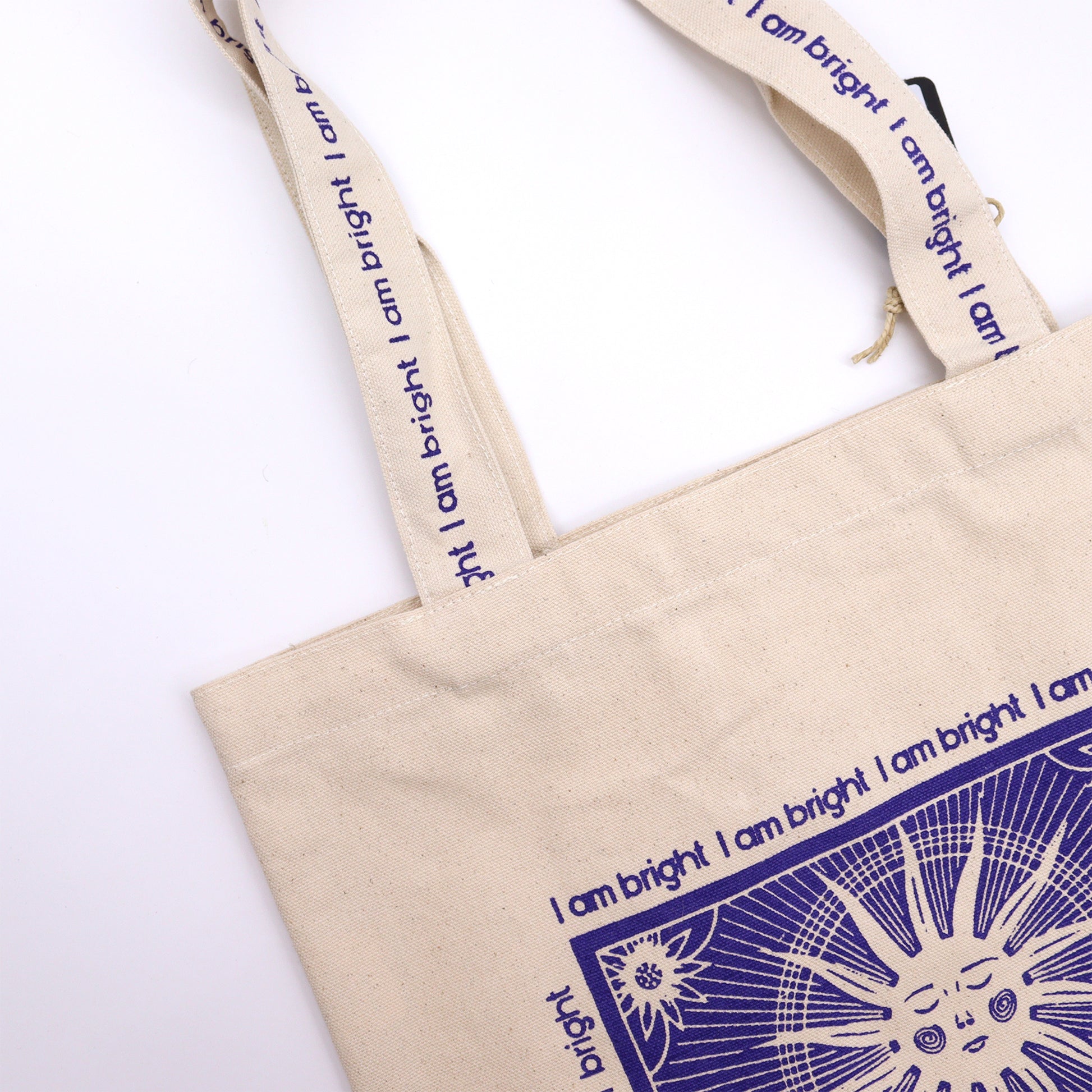 Beige cotton tote bag with print featuring a blue sun design and I am bright text on handles