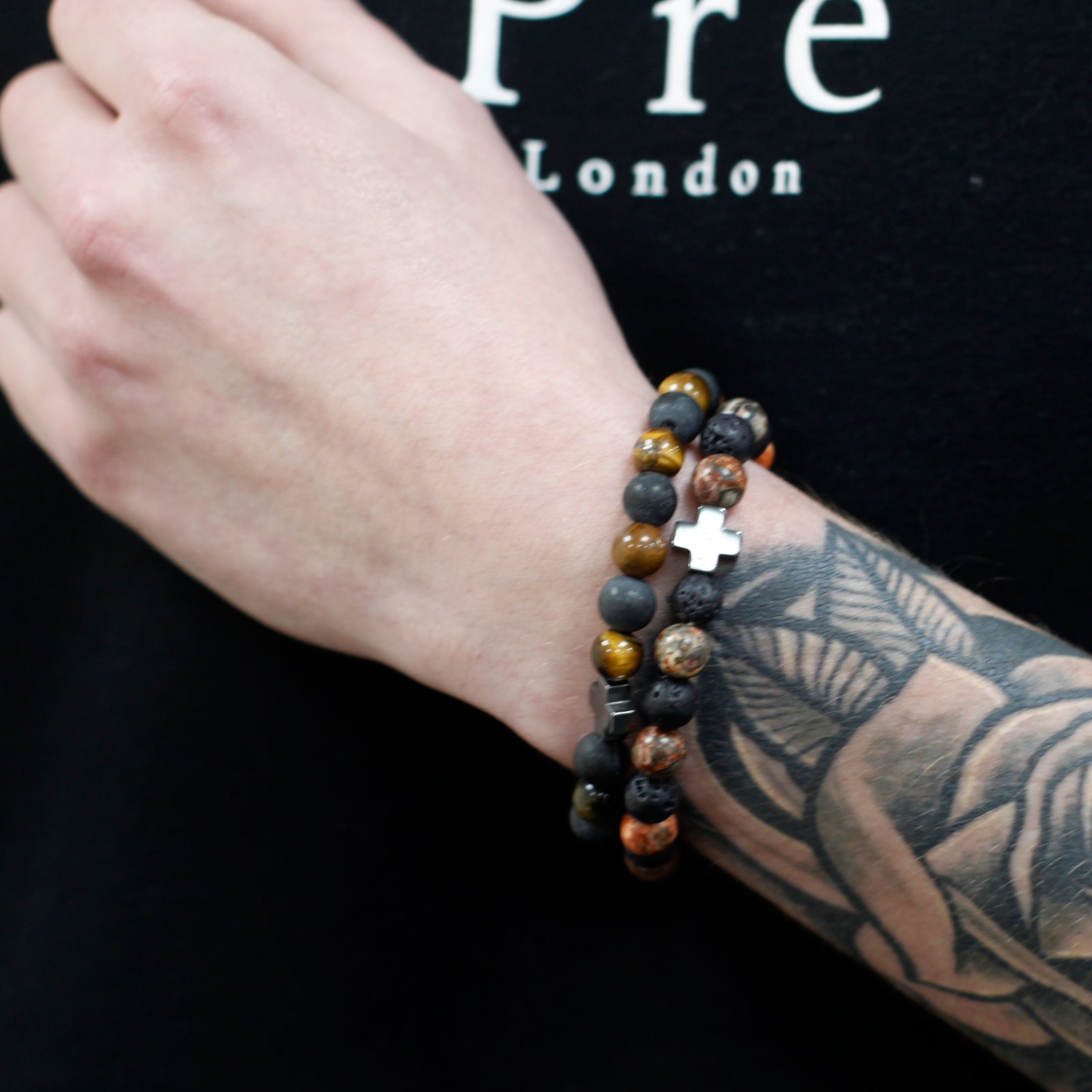 Wrist adorned with gemstone friendship bracelets featuring polished beads and a silver cross charm