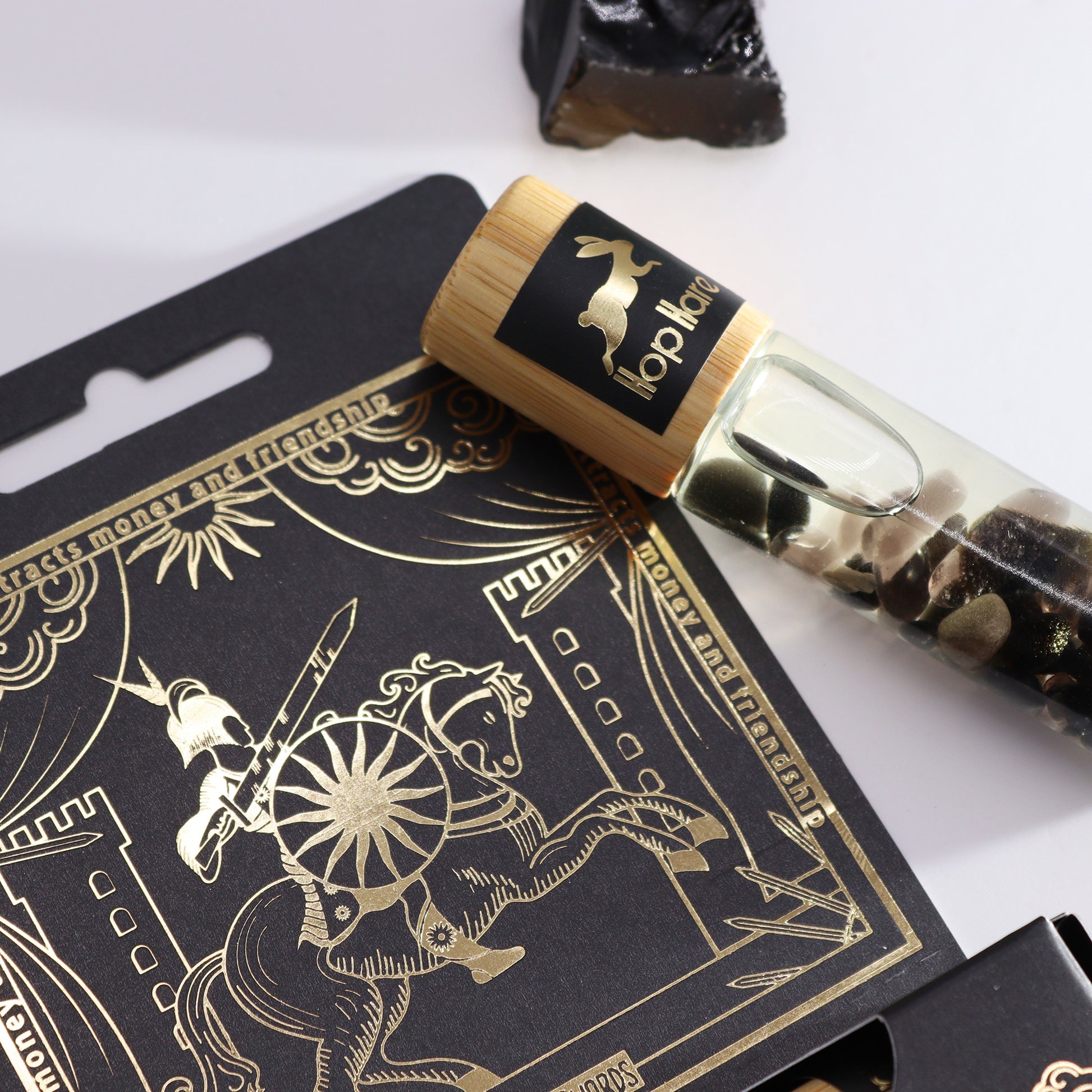 Tarot essential oil roll on bottle with wooden cap and decorative stones beside tarot card packaging