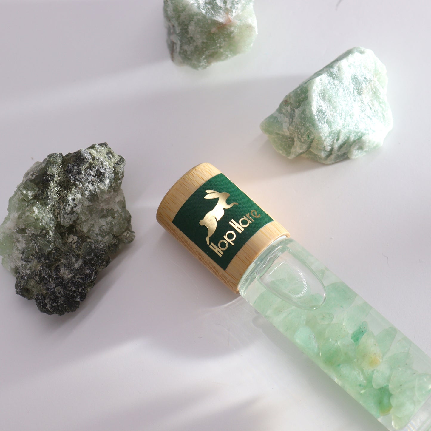 Tarot essential oil roll on with green crystal stones inside and wooden cap on white surface