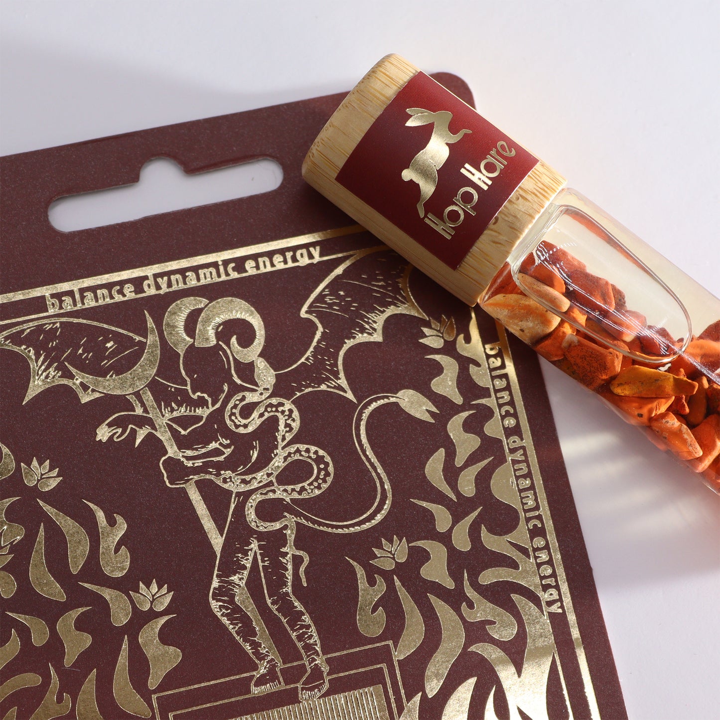 Tarot essential oil roller with orange stones beside a detailed gold and brown tarot card design