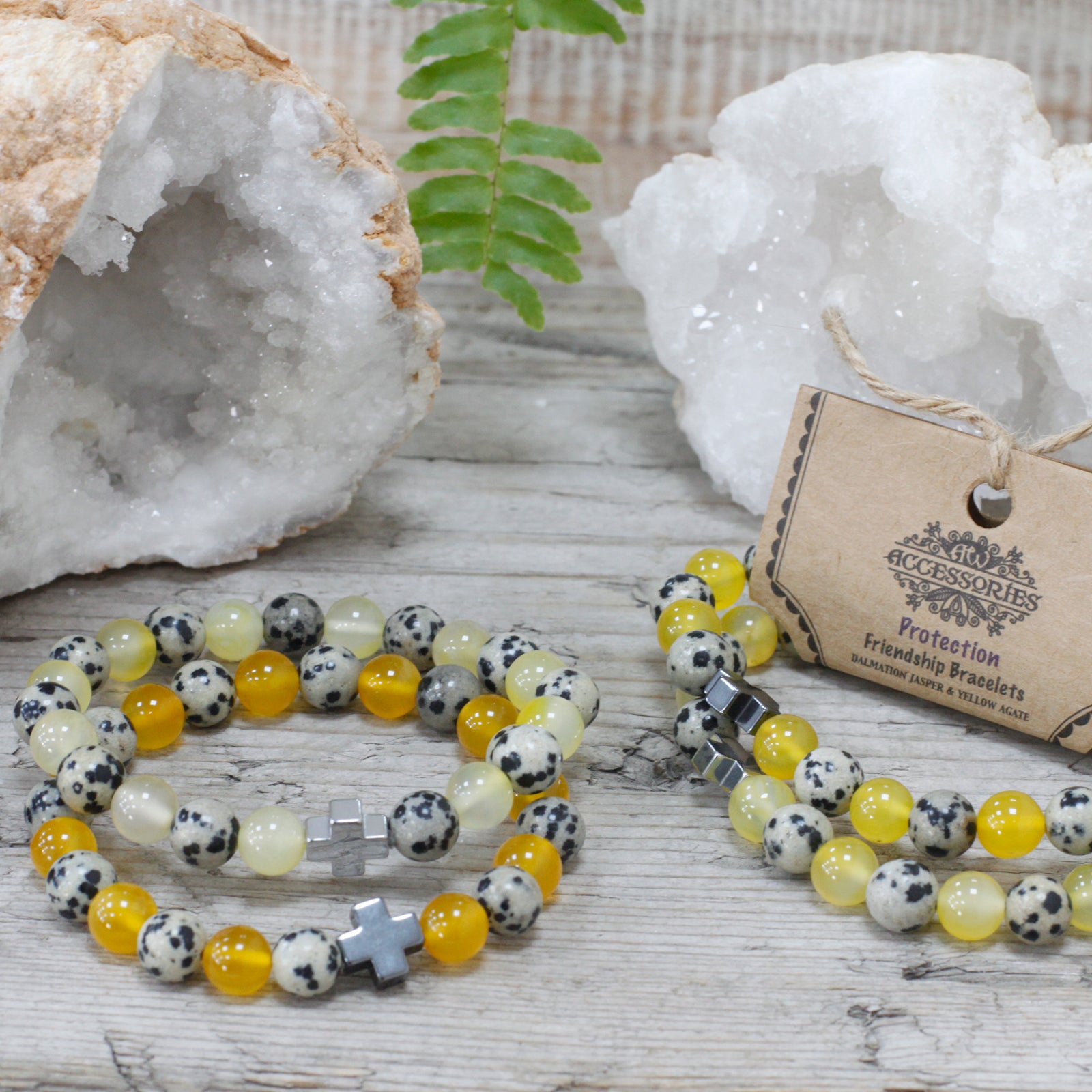 Yellow and spotted gemstone friendship bracelets with cross charms displayed on wooden surface with crystals and fern