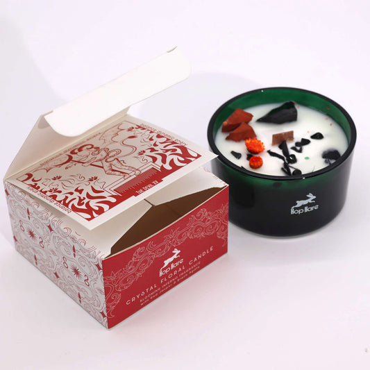 Crystal infused candle in a green glass holder with decorative crystals beside an open red and white packaging box