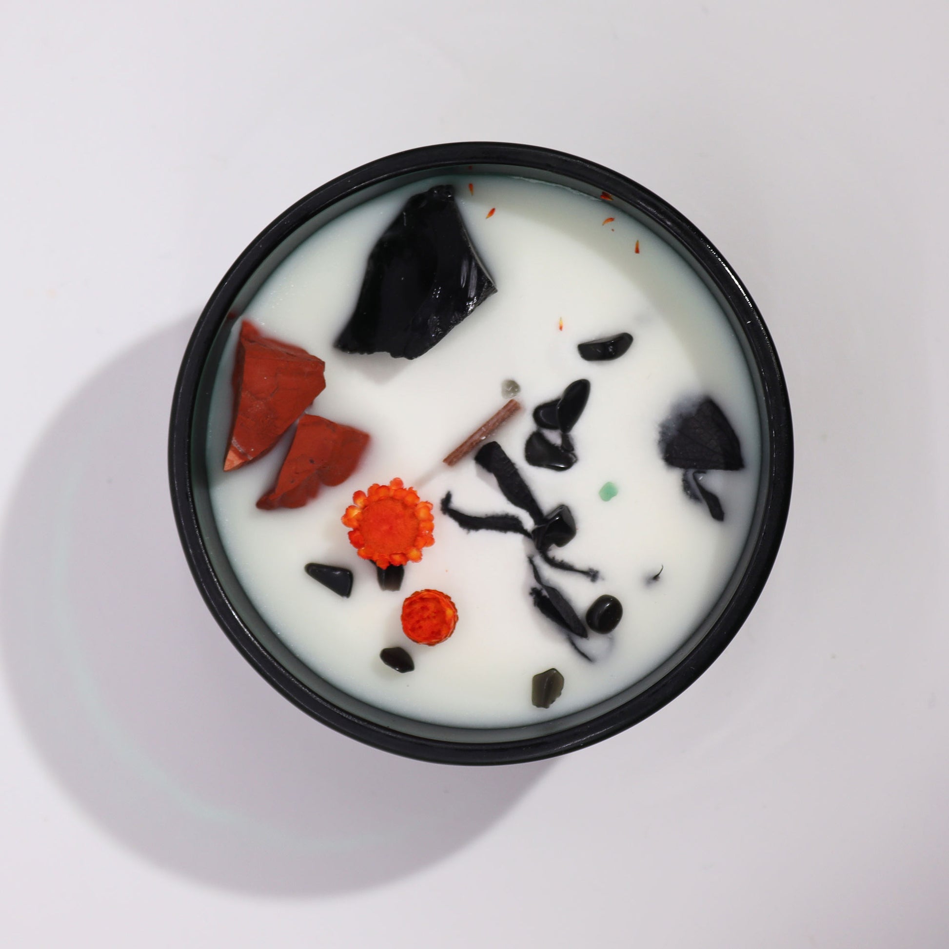 Top view of a crystal infused candle with white wax and embedded black and orange crystals in a black container