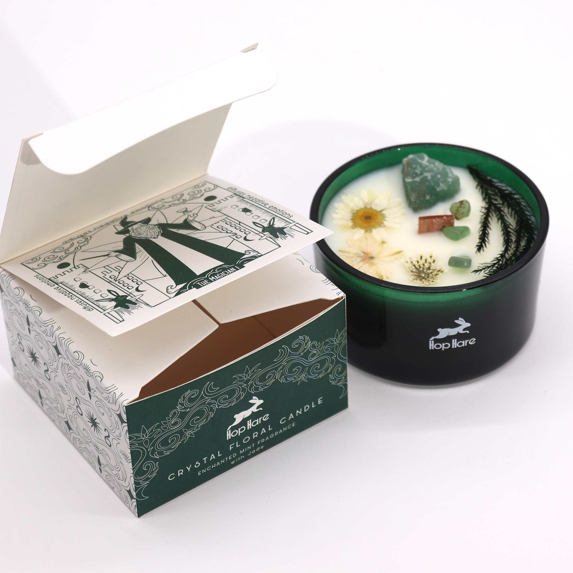 Crystal infused flower candle in green glass container with dried flowers and crystals beside decorative packaging