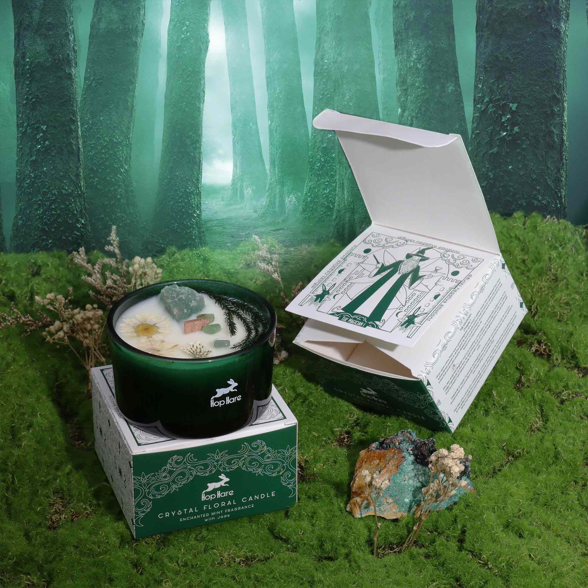 Crystal infused flower candle in a dark green glass jar with floral design box on mossy forest background