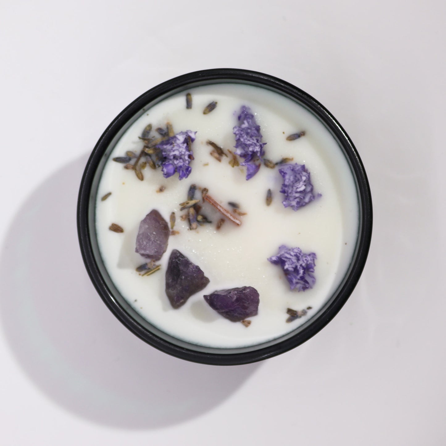 White crystal infused flower candle with purple flowers and crystals in a black container