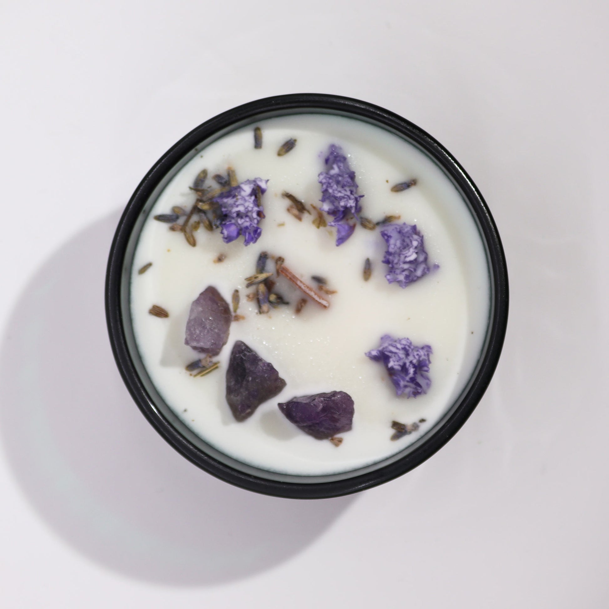 White crystal infused flower candle with purple flowers and crystals in a black container