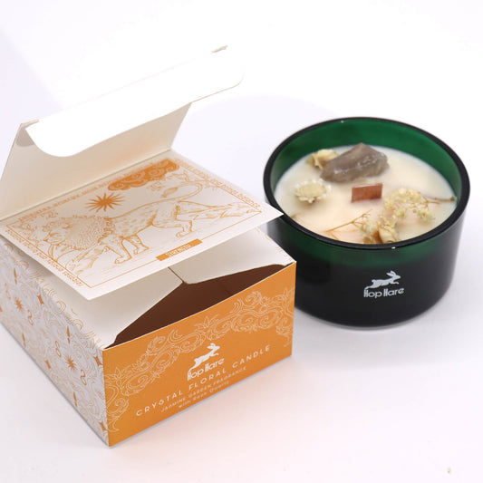 Crystal infused flower candle in a green glass container with dried flowers and crystals alongside decorative orange and white packaging