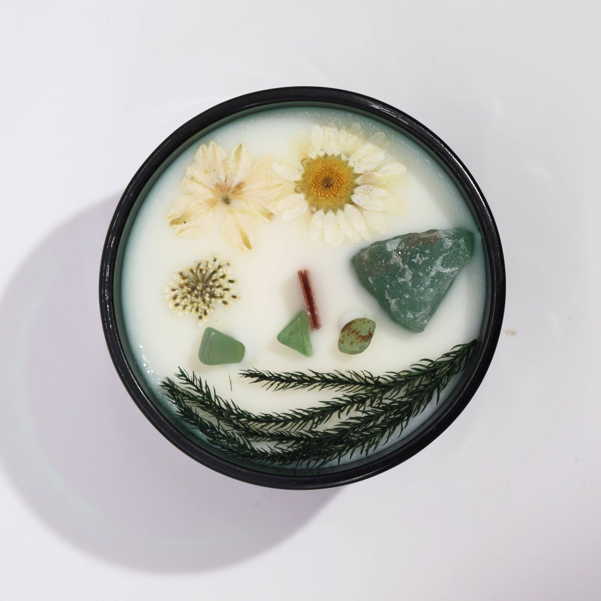 Crystal infused flower candle with dried flowers and green crystals in black container
