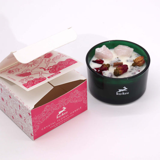 Crystal magic flower candle in green glass container with rose petals and crystals next to decorative pink and white packaging