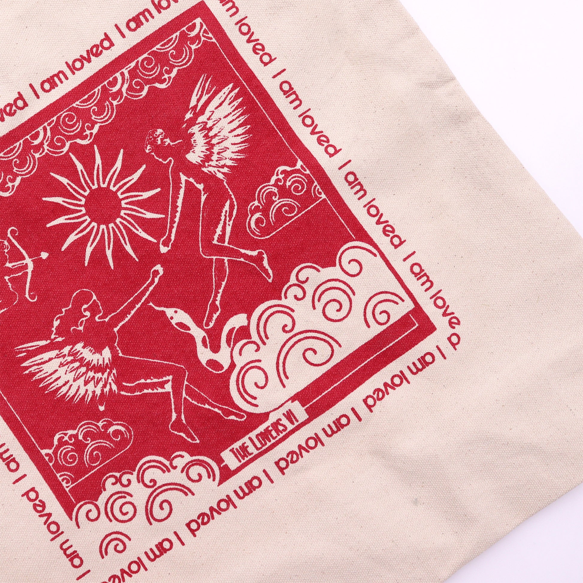 Close-up of beige fabric I am Loved affirmation bag with red angel and sun design print