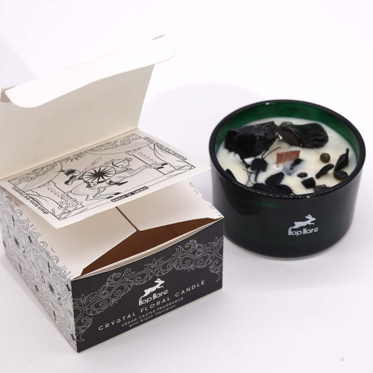 Crystal infused flower candle in a green glass holder with decorative black stones and open packaging