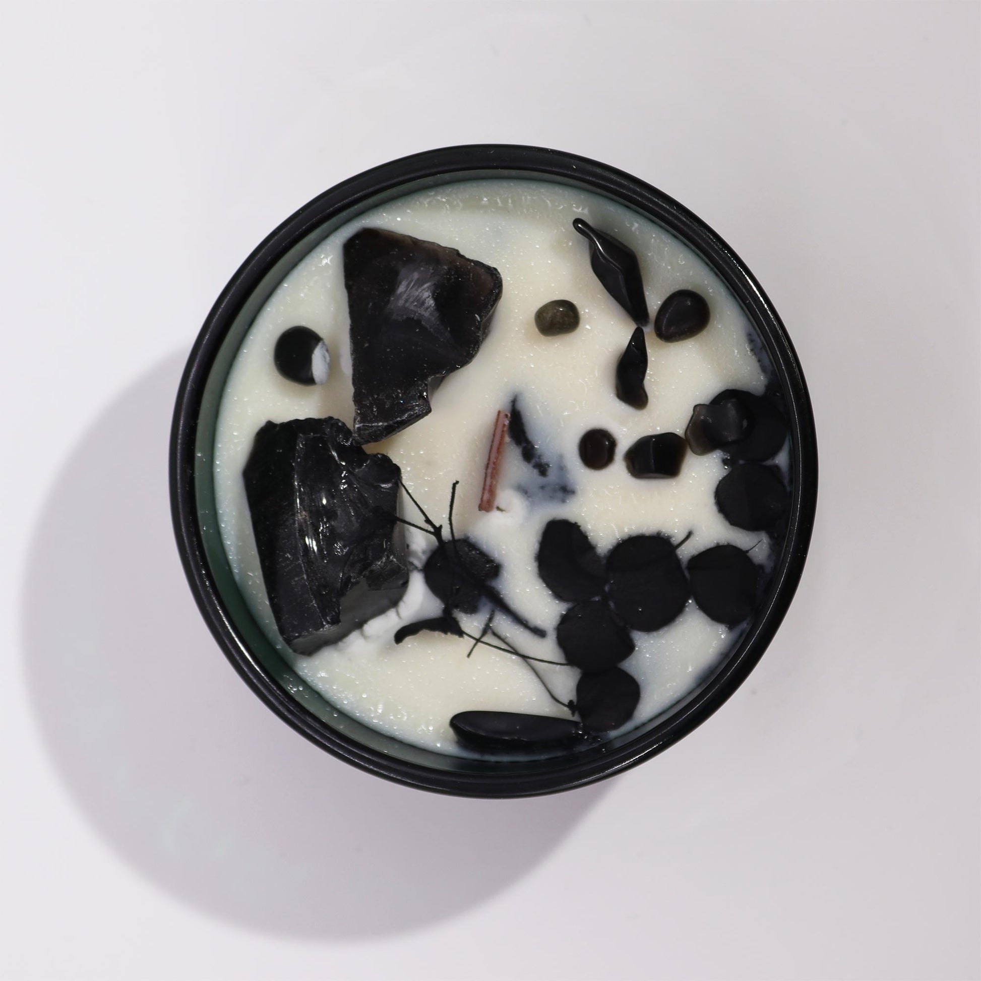 Top view of crystal infused flower candle with black stones and dried petals in white wax