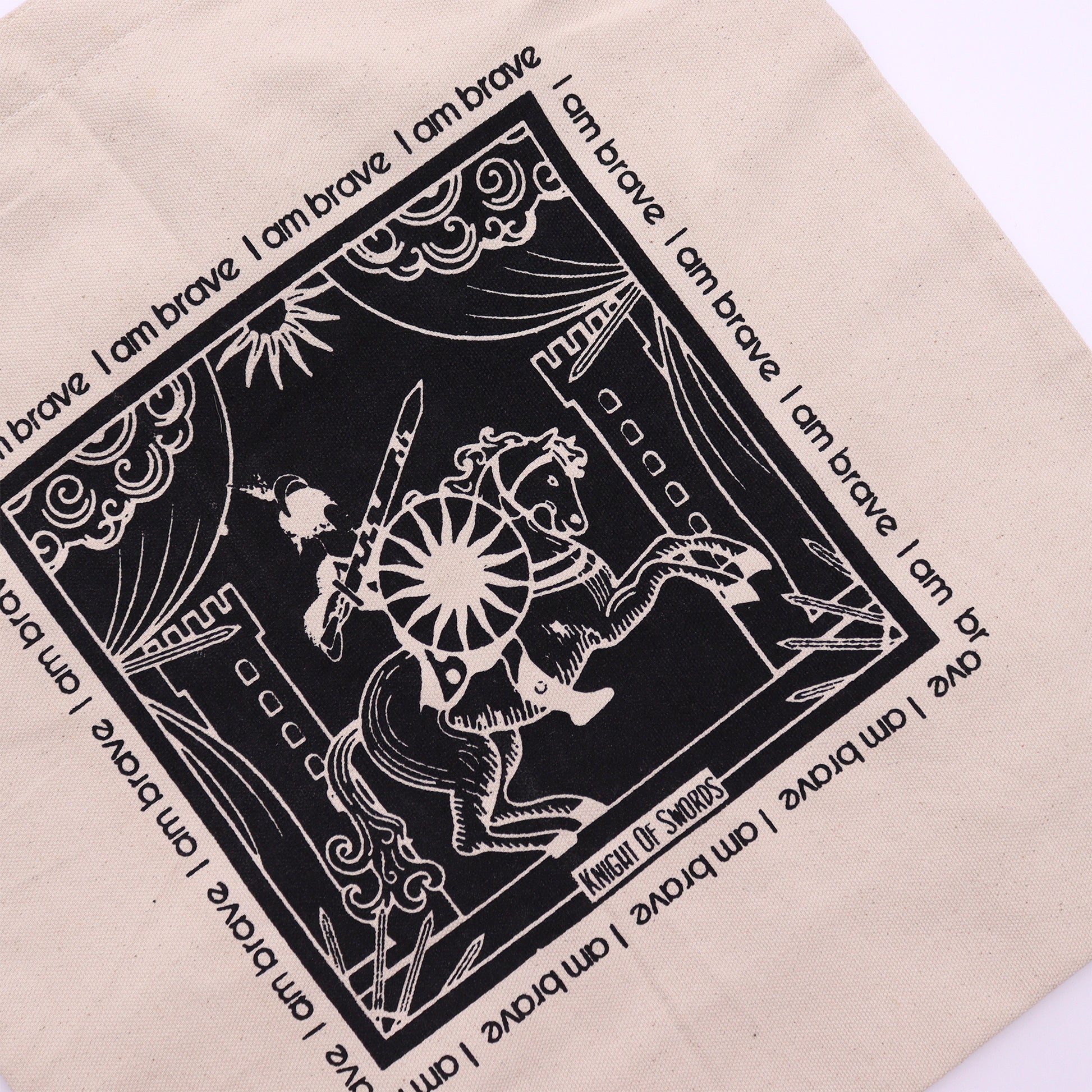 Beige motivational tote bag with black knight of swords design and repeated I am brave text