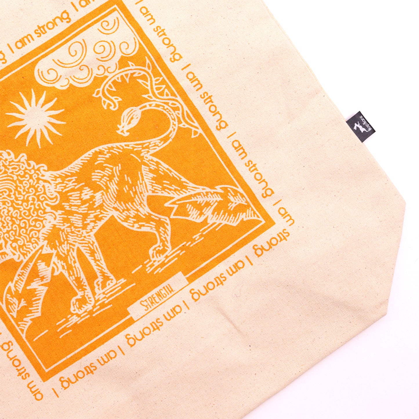 Natural canvas motivational tote bag with orange lion design and repeated I am strong text