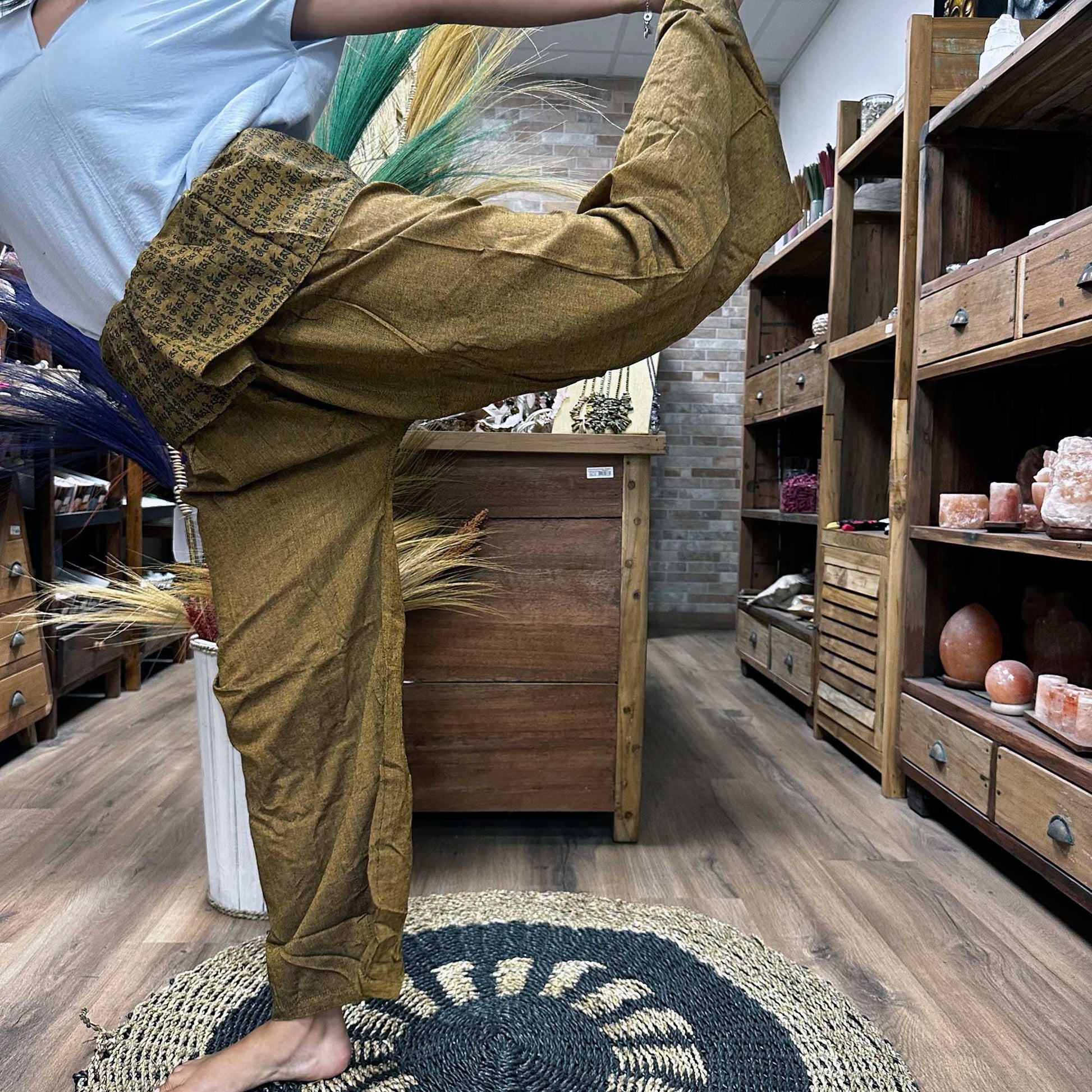 Brown Samsara Wellbeing Thai fisherman pants for yoga worn by person stretching indoors on round rug