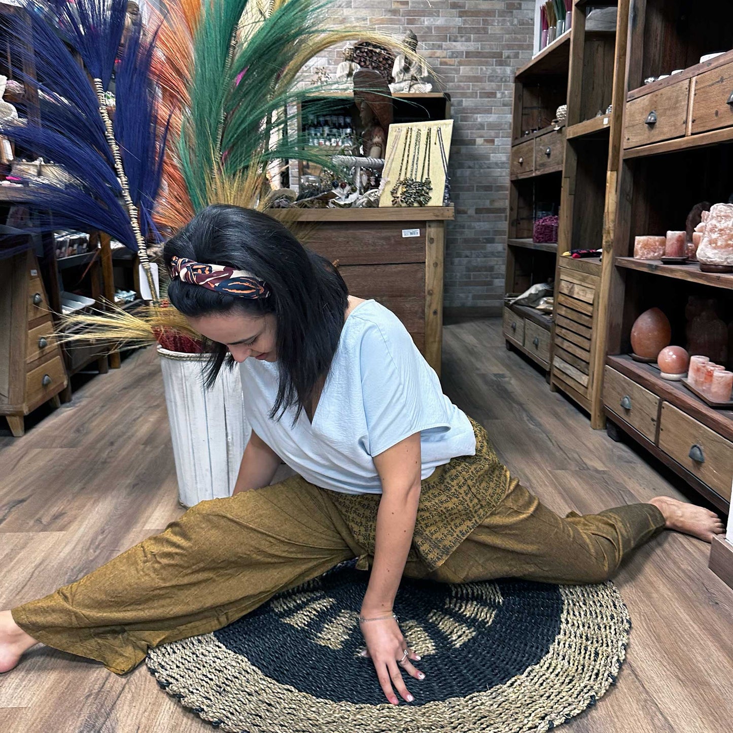 Woman wearing mustard yellow Thai fisherman pants for yoga while stretching indoors on a woven rug