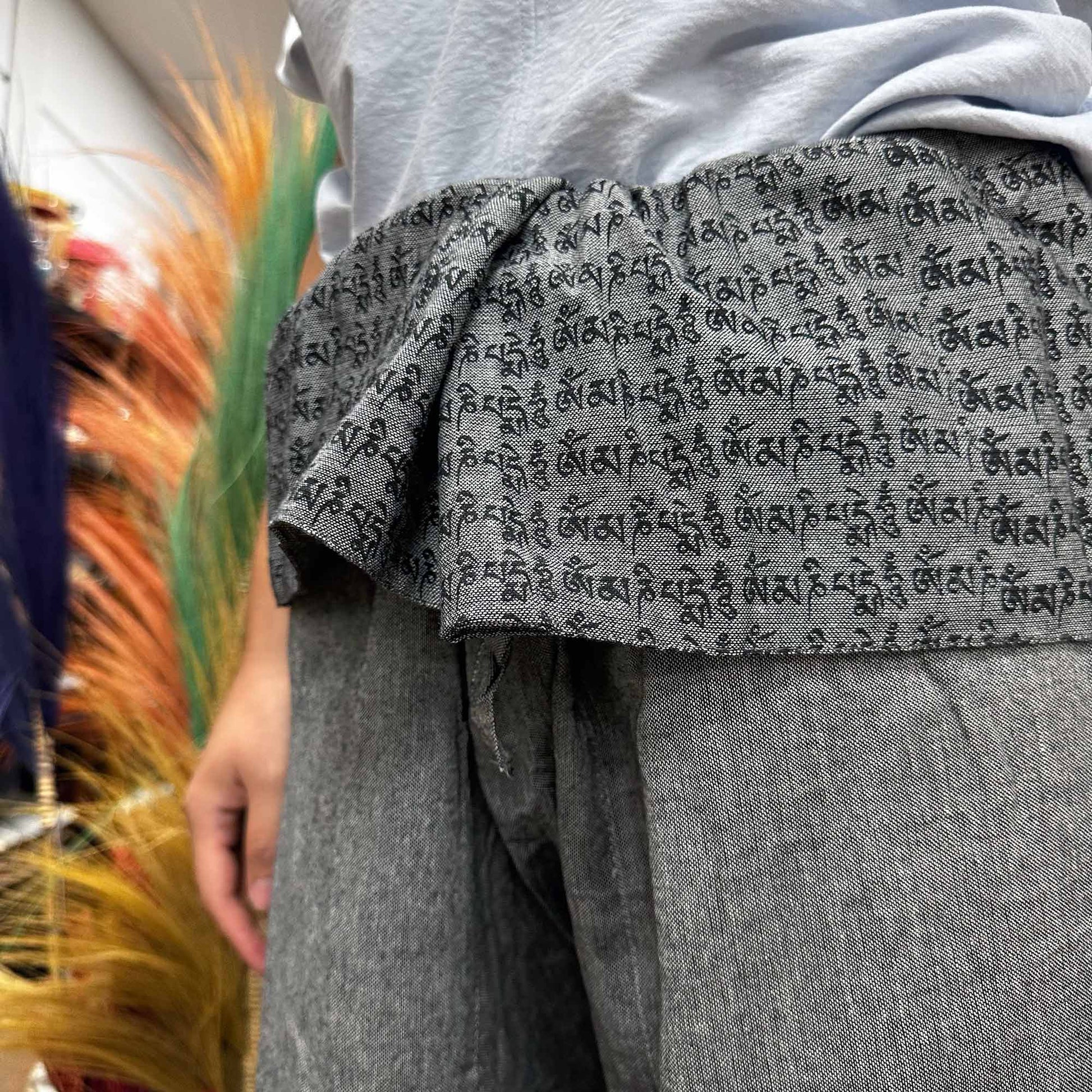 Close-up of grey Samsara Wellbeing Thai fisherman yoga pants with traditional script pattern detail