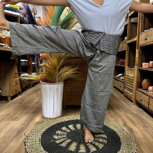 Samsara Wellbeing grey Thai fisherman yoga pants worn by person stretching leg indoors