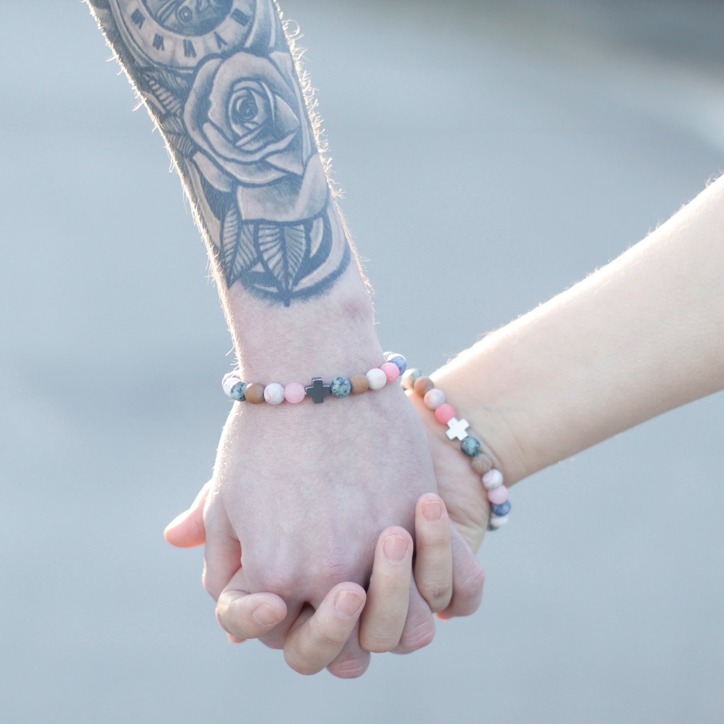 Couple wearing gemstone friendship bracelets set holding hands with visible tattoo on wrist