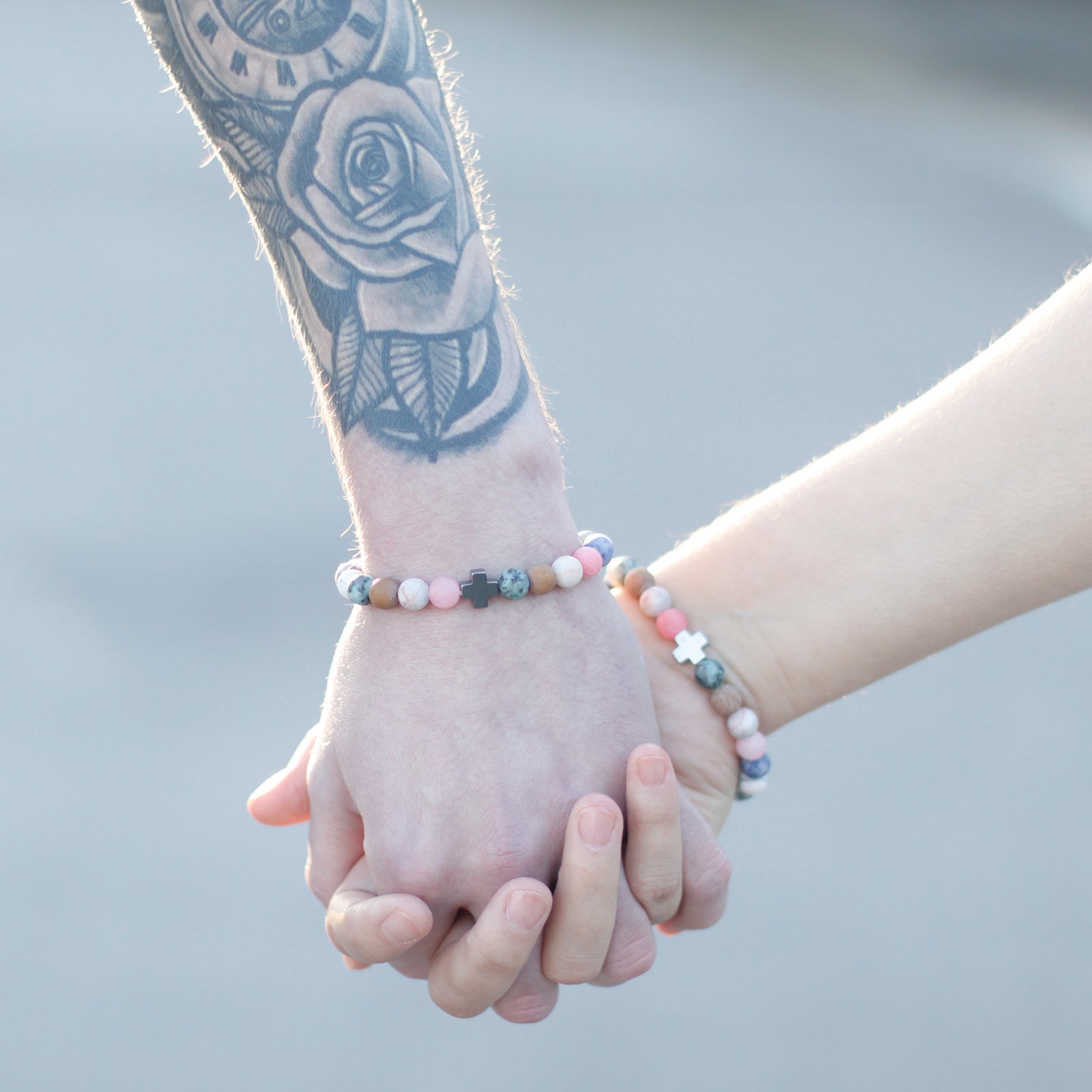 Couple wearing gemstone friendship bracelets set holding hands with visible tattoo on wrist